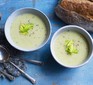 Celery soup in bowl topped with celery leaves, with spoons and bread