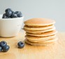 Stack of healthy American pancakes on table with blueberries in bowl