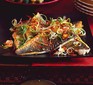 Sea bass fillets with sizzled ginger, chilli & spring onions on a black plate