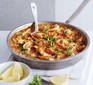Paella in a large pan with serving spoon and lemon wedges