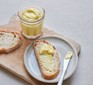 Vegan mayonnaise in a jar, with some spread on a slice of bread alongside